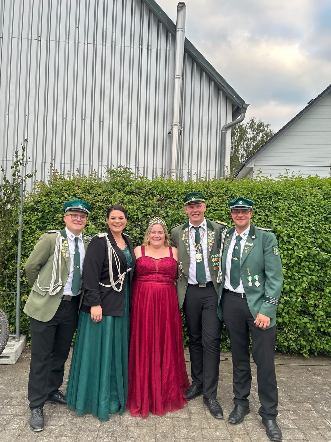 Das Königspaar mit Hofstaat und Adjutanten vor einer Hecke